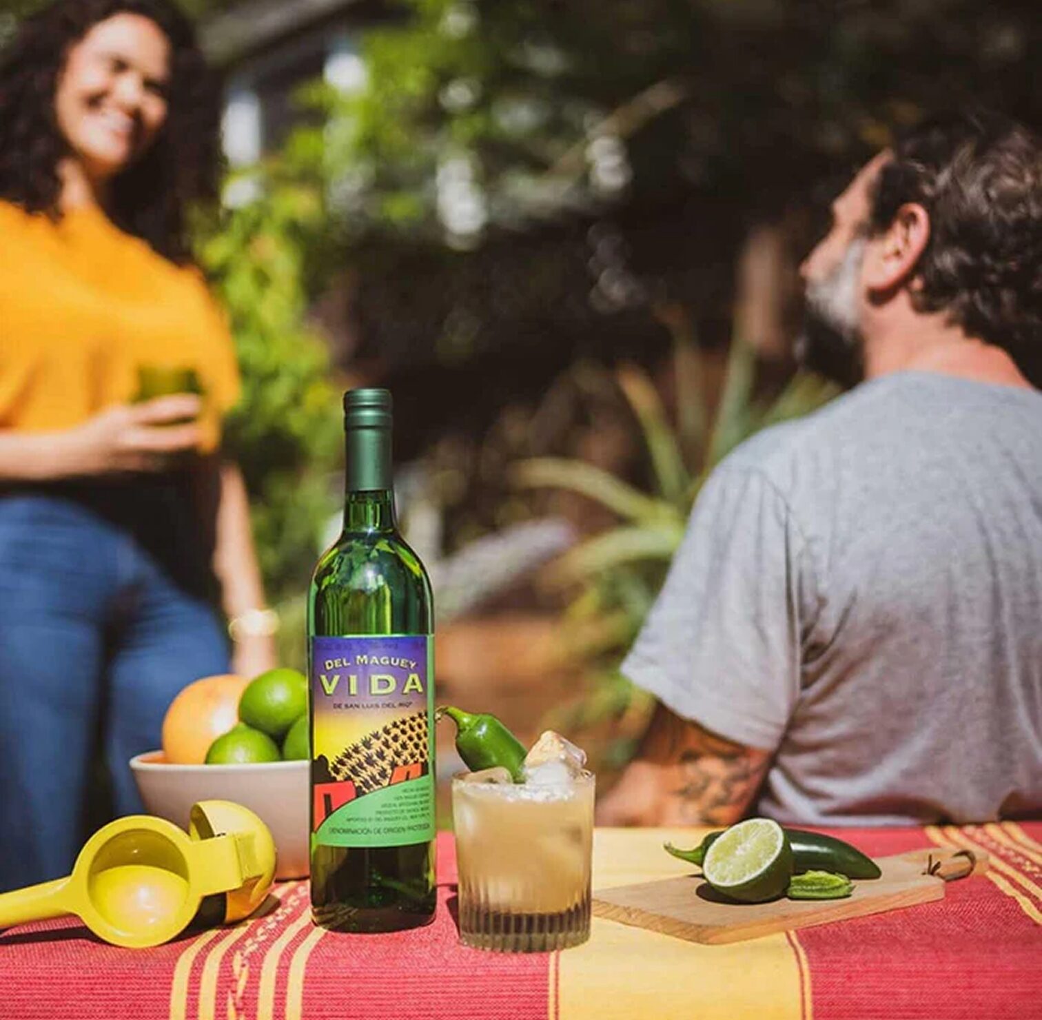 Friends sharing mezcal cocktails outdoors around a Del Maguey Vida bottle