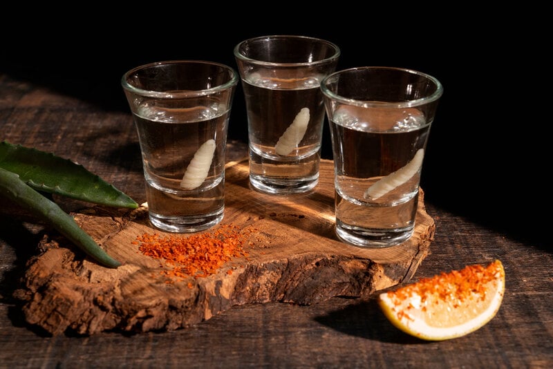 Mezcal tasting flight served in small glasses, accompanied by orange slice and sal de gusano, showcasing a traditional mezcal tasting setup.