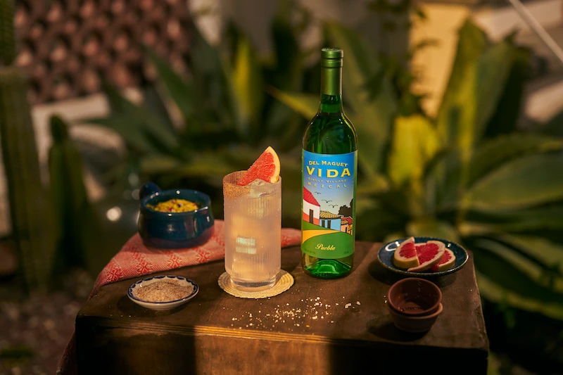 Del maguey vida mezcal bottle with three cocktails served on a refined bar cart with copita and bar tools